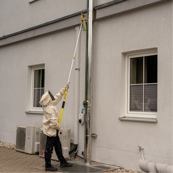 Schädlingsbekämpfer entfernt mit einer Teleskopstange ein Wespennest an einer Hausfassade.